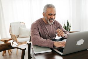 A man smiling and typing on his laptop.