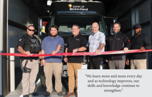 Six men holding red tape across a garage bay titled, "we learn more and more every day and as technology improves, our skills and knowledge continue to strengthen."