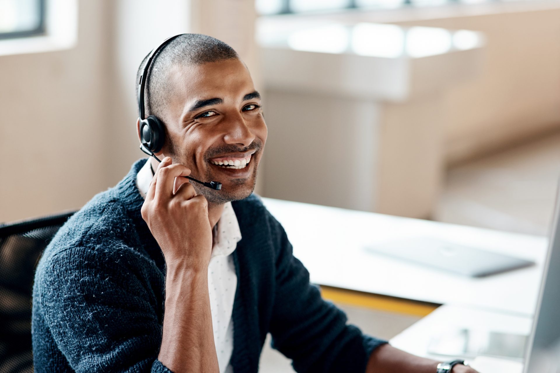 male customer support worker smiles at camera while touching headset