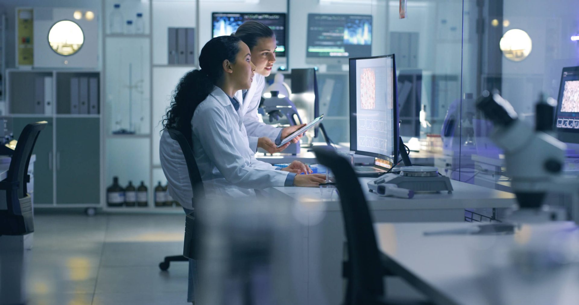 Two women in lab coats observing a computer screen