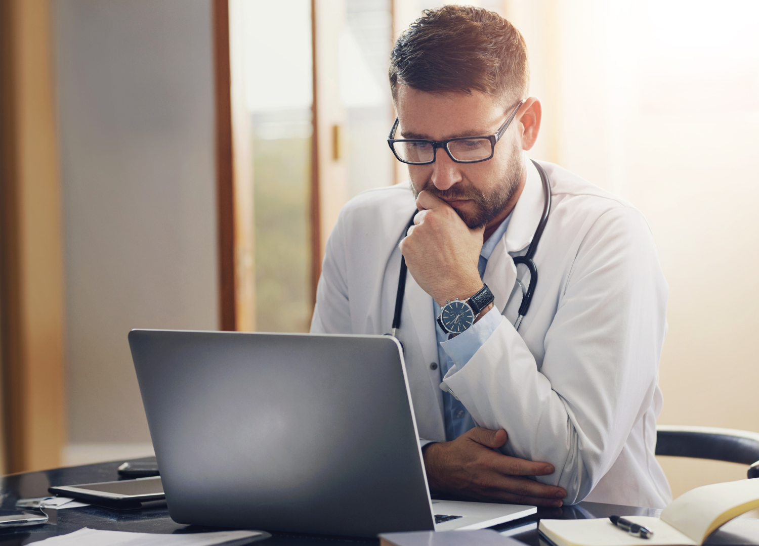 Healthcare professional looking thoughtfully at a laptop while seated at a desk.