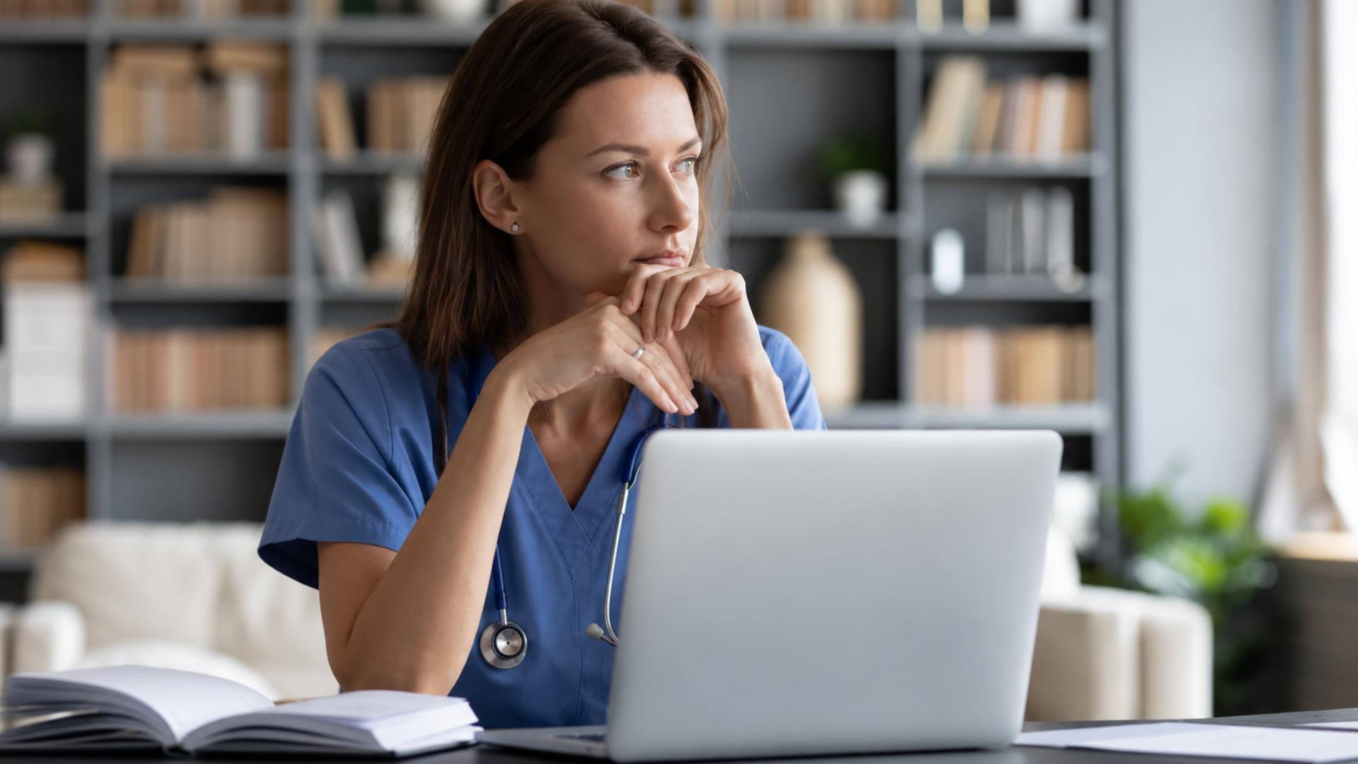 Healthcare professional working on a laptop while reviewing information at a desk.
